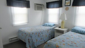 Une chambre avec deux lits, une table de chevet avec une lampe et un climatiseur fixé au mur.