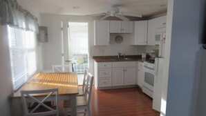 Une cuisine de taille réduite avec des meubles blancs, une table à manger en bois et un ventilateur de plafond.