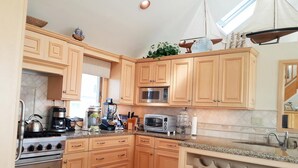 A kitchen with wooden cabinets, a gas stove, a microwave, and a coffee maker. - Beautiful Ocean Front Home Steps To The Beach (Harvey Cedars)