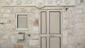 A stone building with two shutters, a small window, and a decorative emblem above the shutters. - Casetta Garibaldi – Studio apartment in the heart of nineteenth-century Ostuni (Ostuni)
