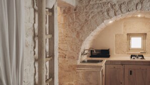 A stone-walled kitchen with a built-in sink, a window, and wooden cabinets. - Casetta Garibaldi – Studio apartment in the heart of nineteenth-century Ostuni (Ostuni)