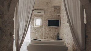 A stone-walled room with a bed, a television, and a window. - Casetta Garibaldi – Studio apartment in the heart of nineteenth-century Ostuni (Ostuni)