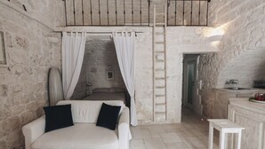 A stone-walled room with a bed, a white couch, a ladder, and a small kitchen area. - Casetta Garibaldi – Studio apartment in the heart of nineteenth-century Ostuni (Ostuni)