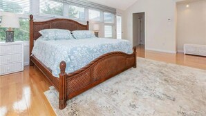 Une chambre à coucher avec un grand lit, une tête de lit en bois, une commode blanche et une fenêtre avec des stores.