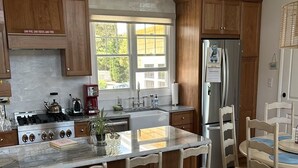 A modern kitchen with wooden cabinets, a central island with bar stools, a refrigerator, and a dining area with a sofa. - 4 bedroom accommodation in Loveladies (Loveladies)