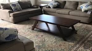 A living room with a beige sectional sofa, a wooden coffee table, and a patterned rug.