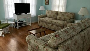 Ein Wohnzimmer mit Fernseher, floralem Sofa, zwei Lampen und einem Bilderrahmen an der Wand.