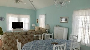 Ein Wohnzimmer mit einer Couch, einem Esstisch mit Stühlen, einem Fernseher, einer Kandelaber und einem Schrank.