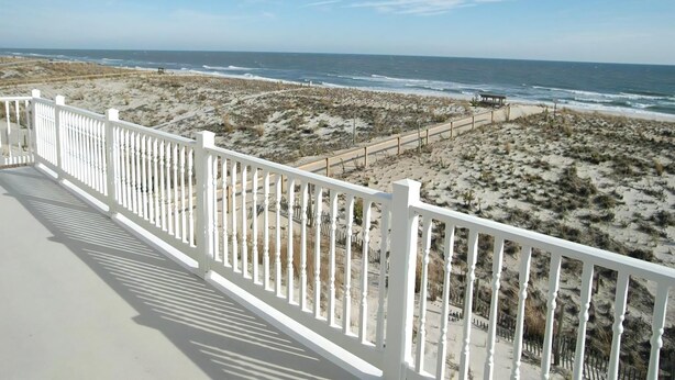 Un balcon doté d’une balustrade blanche, donnant sur une plage bordée de dunes et sur l’océan.