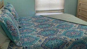 Une chambre à coucher avec un lit, une fenêtre avec des stores et une commode.