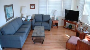 Un salon comprenant un canapé, une table basse, un téléviseur et une petite table en bois avec une lampe.