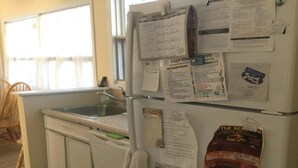 A kitchen with a sink, a refrigerator, and various papers and notices on the fridge. - CLASSIC LAGOON FRONT HOME (Loveladies)