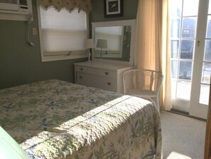 Quarto com cama, cômoda, cadeira, janela e telefone fixado na parede.