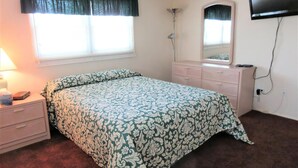 A bedroom with a bed, a dresser, a mirror, a TV, and a lamp.