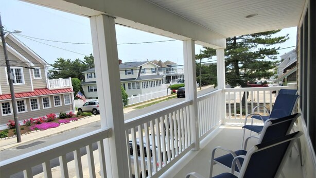 A covered porch with white railings and blue chairs.