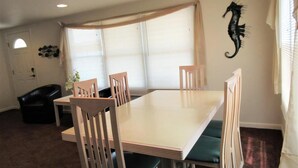 A dining area with a table, chairs, a black leather sofa, a decorative seahorse, and a window with blinds.