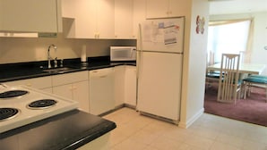 A kitchen with white cabinets, a microwave, a refrigerator, a stove, and a dining area with a table and chairs.
