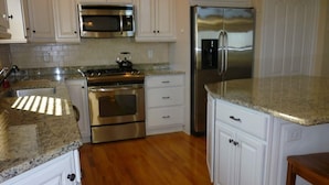 A kitchen with white cabinets, stainless steel appliances, granite countertops, and wooden flooring. - 220 12th St Associates, LLC (Beach Haven)