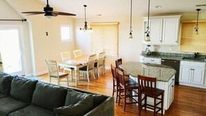 A modern kitchen with white cabinets, a granite countertop, and a dining area with wooden chairs. - 220 12th St Associates, LLC (Beach Haven)