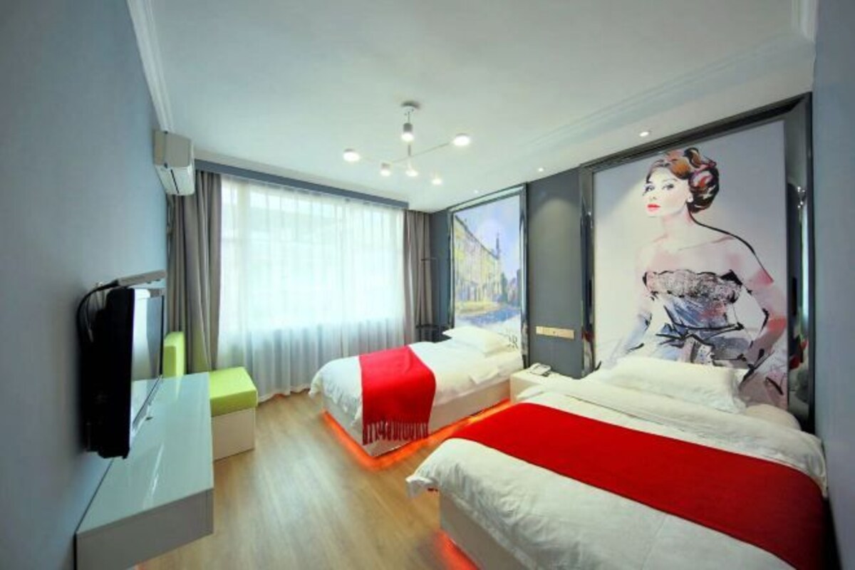 A hotel room with two beds, a TV, a large window, and a painting on the wall.