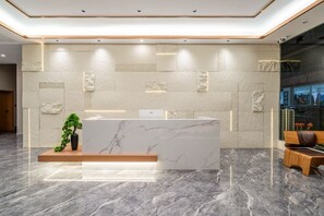 A reception area with a marble counter, a potted plant, and a seating area with a bench and a table. - Yin E Hotel (Emeishan City)
