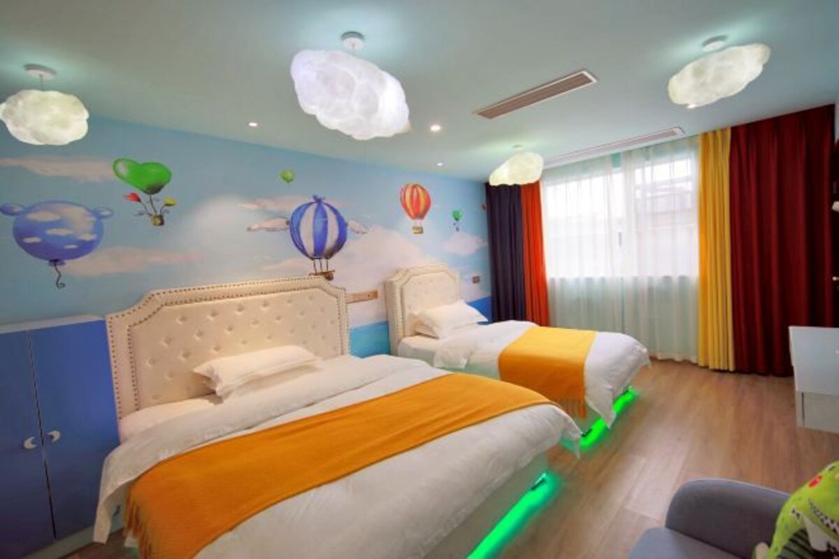 A hotel room with two beds, a large window with curtains, and a wall mural of hot air balloons.