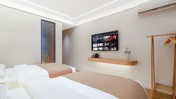 Una habitación de hotel moderna con una cama grande, un televisor de pared, un armario de madera y un estante pequeño con artículos de aseo.