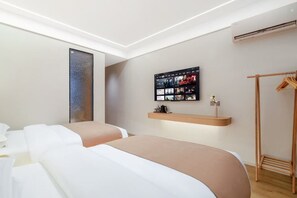 A modern hotel room with a large bed, a wall-mounted TV, a wooden wardrobe, and a small shelf with toiletries. - Yin E Hotel (Emeishan City)