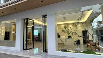 A modern building with glass doors, a visible interior with seating and a plant, and a clear view of the street outside.