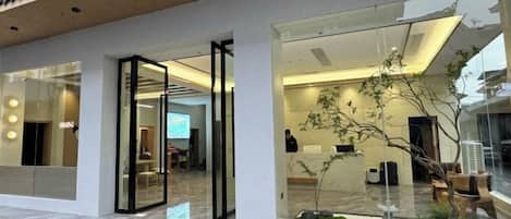 A modern building with glass doors, a visible interior with seating and a plant, and a clear view of the street outside.
