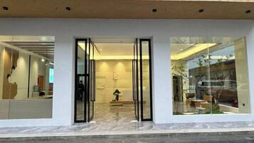 A modern building entrance with glass doors, a tiled roof, and a visible interior with furniture.