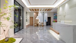 A modern reception area with a marble floor, a reception desk, and a plant. - Yin E Hotel (Emeishan City)
