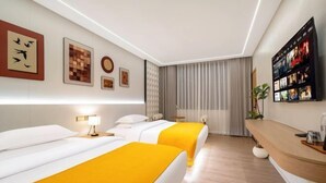 A hotel room with two beds, a TV, a desk, and artwork on the walls. - Yin E Hotel (Emeishan City)
