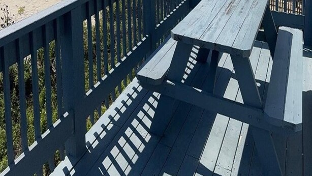 A wooden deck with picnic tables overlooking a beach with sand dunes.