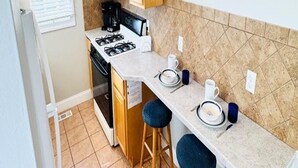 A compact kitchen with a gas stove, a coffee maker, and a microwave. There are two stools and a small bar counter.