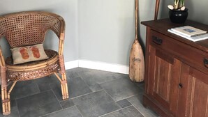A corner room with a wicker chair, a wooden cabinet, a potted plant, a broom, and a wall decoration.