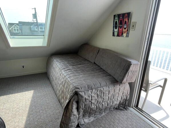 A small, single-bed room with a sloped ceiling, a window, and a door.