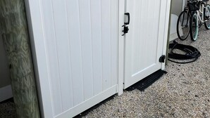 A white gate with a black handle, a bicycle, and a white object on gravel.