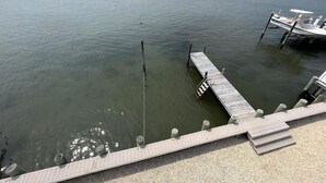A calm body of water with a dock extending into it, a boat moored at the dock, and a distant shoreline.