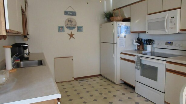 A compact kitchen with a refrigerator, microwave, oven, and sink. There is a ceiling fan, a small cabinet, and a decorative star on the wall. - Nice townhouse style condo with pool in Brant Beach. Unit overlooks pool and. (Brant Beach)