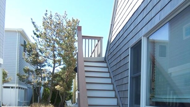 Un escalier menant à un palier du deuxième étage, situé à côté d’un bâtiment doté d’une fenêtre et d’un revêtement extérieur.