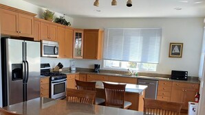 Une cuisine moderne avec des meubles en bois, des appareils en acier inoxydable, un plan de travail en granit et un coin repas avec des chaises en bois.