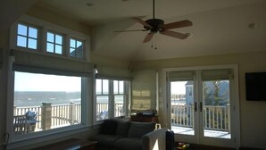 A spacious room with large windows, a ceiling fan, and a balcony with a view of the ocean.