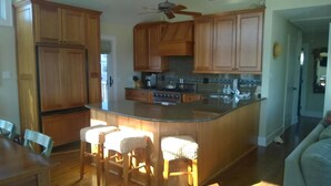 A kitchen with wooden cabinets, a central island with stools, a stove, and a ceiling fan.