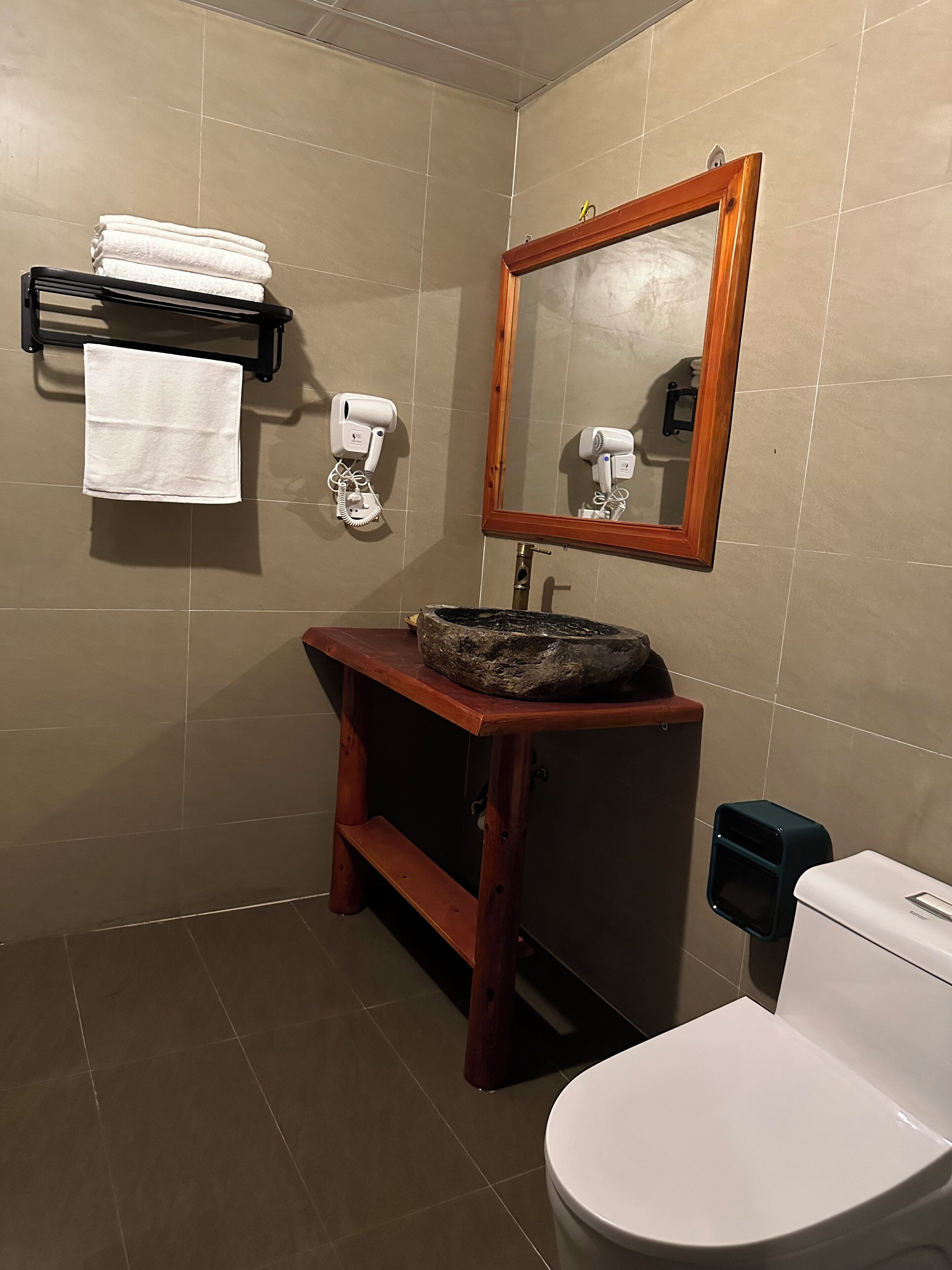 Un baño con tocador de madera, un lavabo con pileta de piedra, inodoro, espejo con marco de madera y toallero con toallas dobladas.