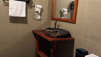 Ein Badezimmer mit Holzwaschtisch, einem Becken aus Stein, Toilette, Spiegel mit Holzrahmen und Handtuchhalter mit gefalteten Handtüchern.