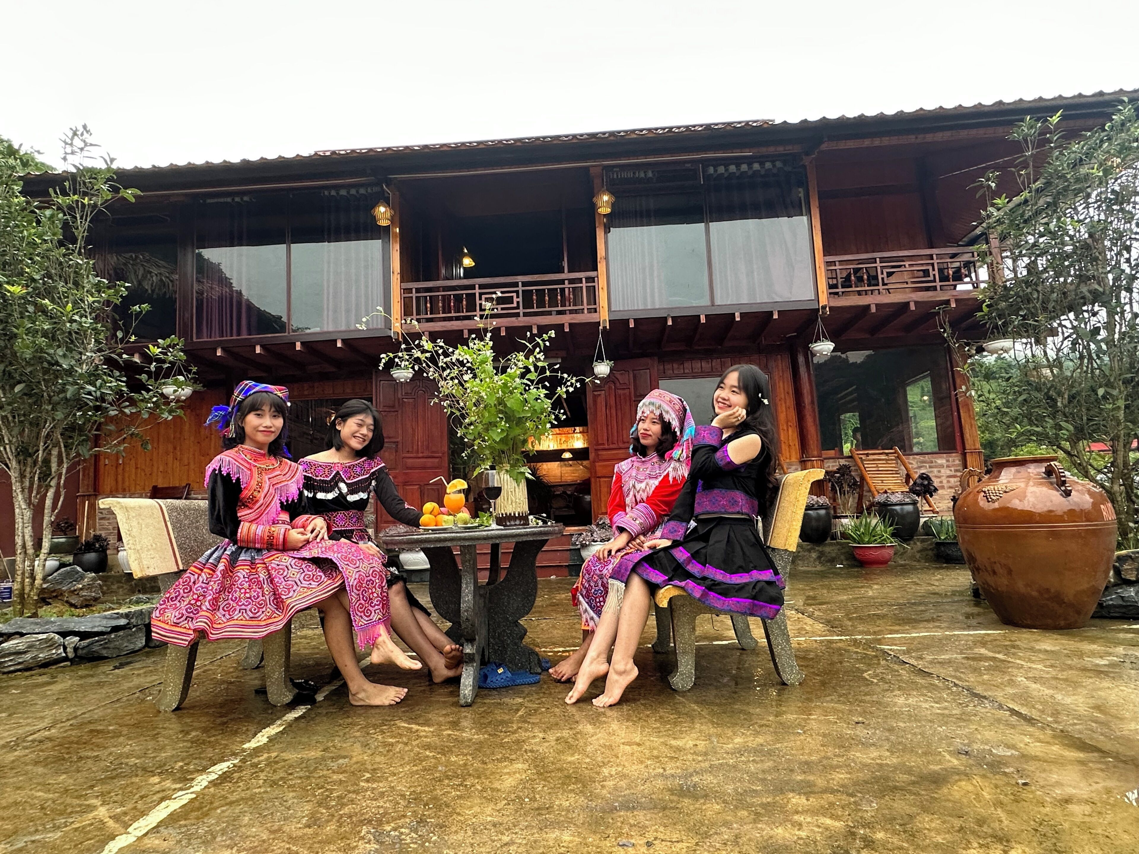 A traditional wooden house with a balcony, a table with a vase of flowers, and potted plants.