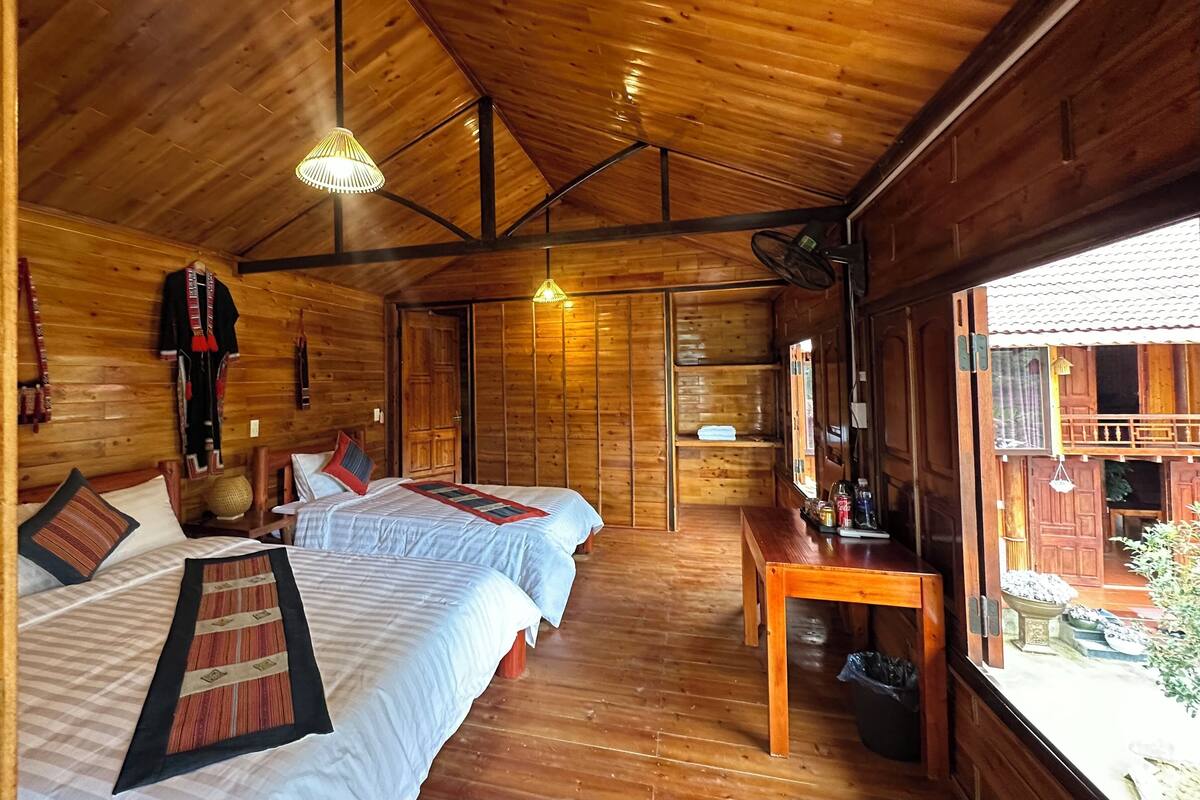 A wooden cabin with two beds, a table, and a window with a view of the outside.