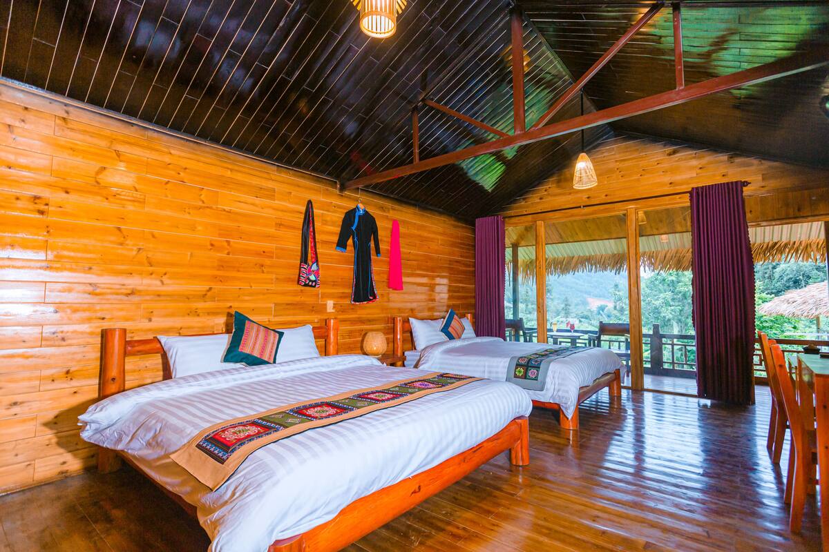 A wooden cabin with two beds, a large window, and a dining area.