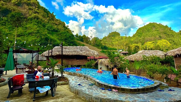 A pool area with thatched-roof huts, outdoor seating, and a mountainous backdrop. - Bac Ha Lodge Reatreat (Bac Ha)